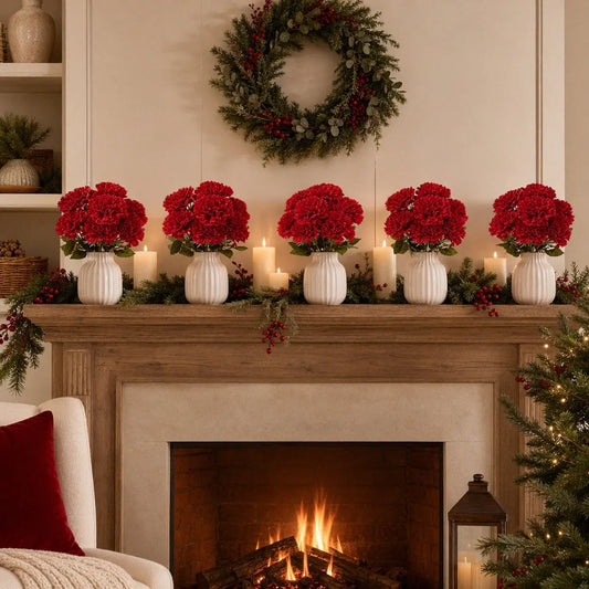 Artificial red carnation flowers in white vases arranged on fireplace mantel with candles and holiday wreath, Christmas home décor