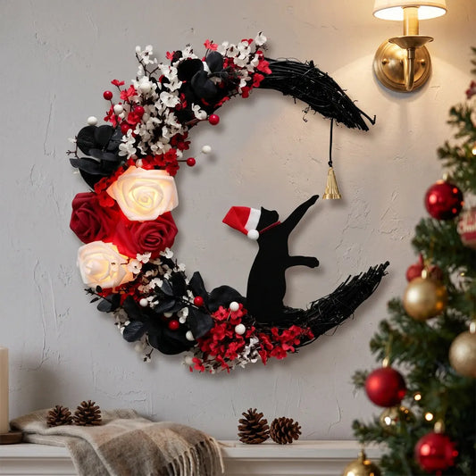 Christmas crescent moon black cat wreath with Santa hat cat silhouette, white and red roses, red berries and gold jingle bell, displayed on wall beside a lit gold sconce with Christmas tree in background