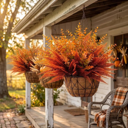 Orange artificial Boston fern bush bundles displayed in hanging wire baskets on a farmhouse porch with pumpkins and autumn foliage