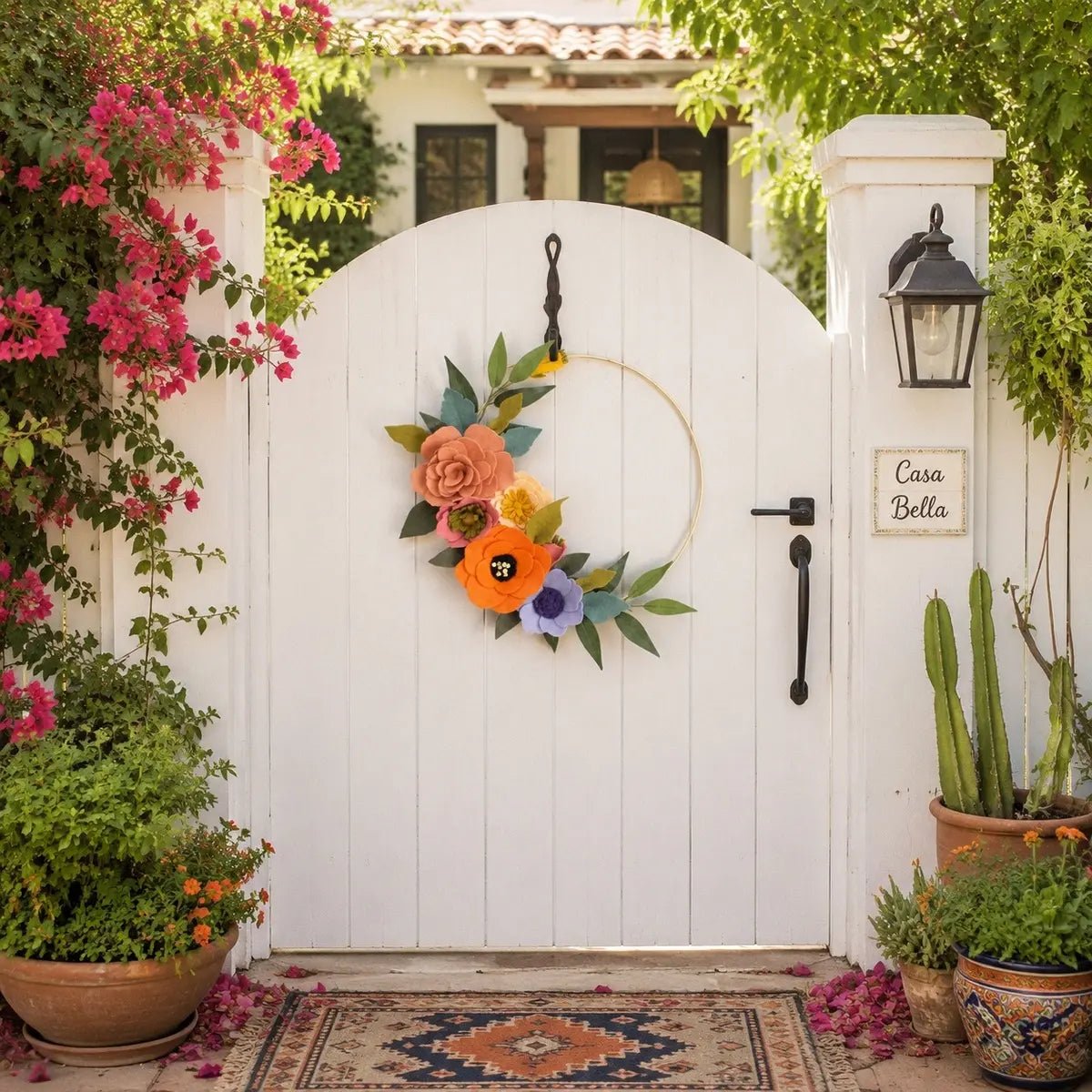 Artificial floral hoop wreath with orange and pink flowers hanging on white arched garden gate
