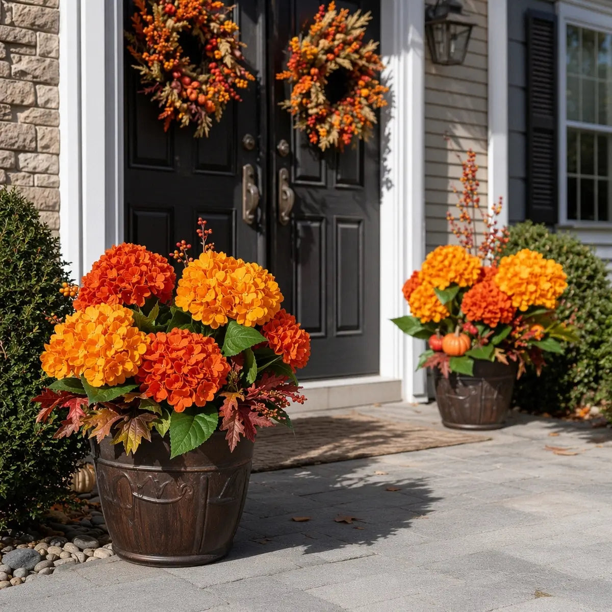 Artificial orange hydrangea stems arranged in a black planter on front porch steps with pumpkins and autumn decor