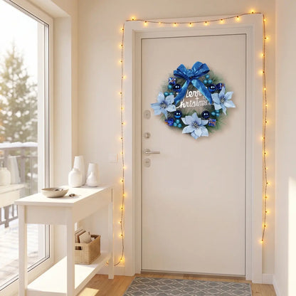 Artificial Christmas wreath with blue bow and white poinsettias hung on a white front door, surrounded by warm fairy lights in a bright entryway
