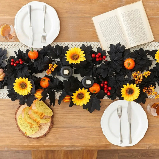 Black autumn garland with yellow sunflowers, orange pumpkins, and red berries used as a table runner on a wooden dining table with white plates, candles, and bread board for Thanksgiving harvest table decor