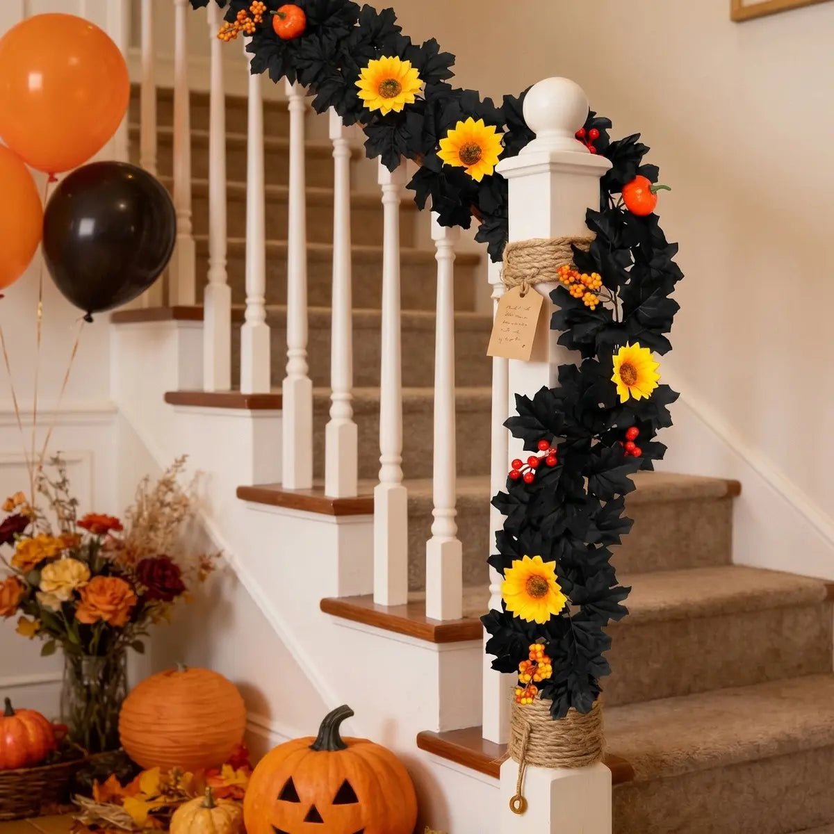 Black fall garland with yellow sunflowers, orange pumpkins, and red and orange berries wrapped around a white staircase banister with orange and black balloons, jack-o-lanterns, and fall flowers for Halloween party decor