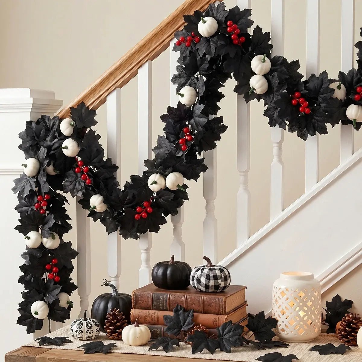 Black maple leaf garland with white pumpkins and red berries wrapped around a white staircase banister with black pumpkins, pine cones, skull, and candle lantern for Halloween home decor