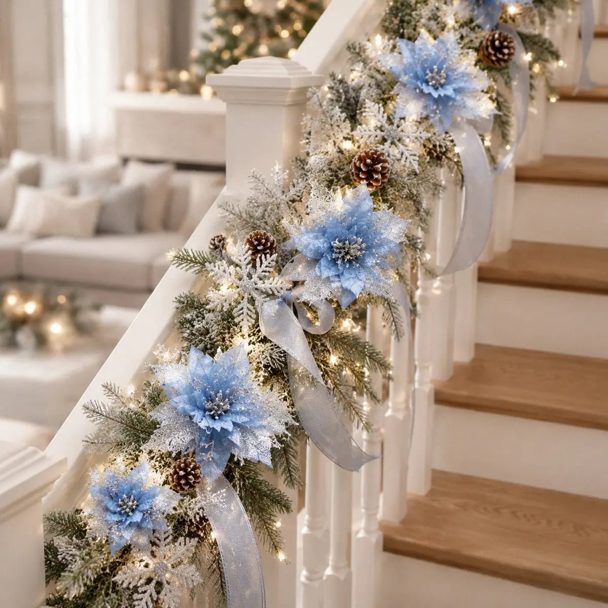 Light blue glitter artificial poinsettia picks clipped onto a frosted pine staircase garland with natural pinecones, white glitter snowflake ornaments and a sheer silver ribbon bow, draped along a white painted wood staircase railing with warm fairy lights, in a bright neutral Scandinavian-style Christmas living room with a fully decorated flocked Christmas tree in the background
