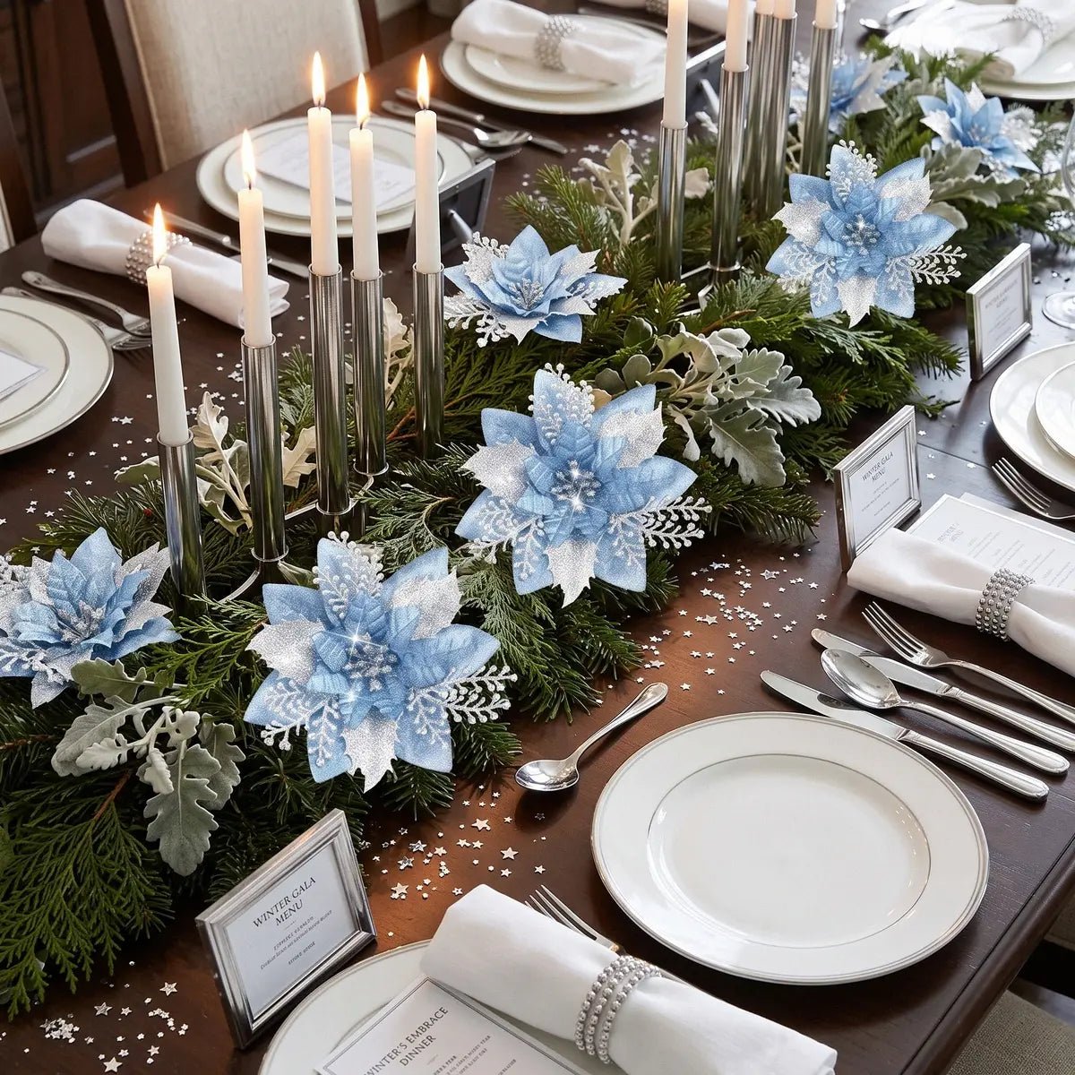 Light blue glitter artificial poinsettia picks arranged in a pine and dusty miller table centerpiece garland runner on a dark walnut dining table, styled with silver taper candles in modern silver candlestick holders, white porcelain place settings with silver napkin rings and silver star confetti, for a Winter Gala dinner party