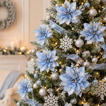 Light blue glitter artificial poinsettia picks with silver glitter centers clipped onto a frosted Christmas tree, styled with silver ball ornaments, white glitter snowflake ornaments and sheer silver ribbon, with a white marble fireplace and lit pine garland in the background of a warm cream living room
