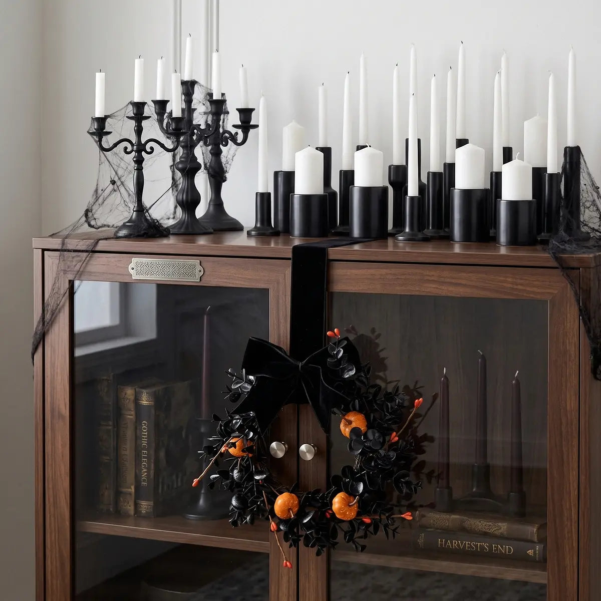 Gothic Halloween mini wreath with black bow and pumpkins displayed on a dark wooden cabinet with candles and Halloween styling
