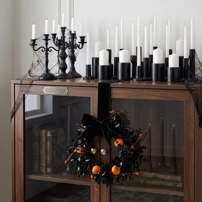 Gothic Halloween mini wreath with black bow and pumpkins displayed on a dark wooden cabinet with candles and Halloween styling