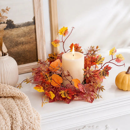 Fall maple leaf candle ring wreath with mixed red orange and yellow leaves and twig sprigs arranged around a pillar candle on a marble surface with autumn home decor