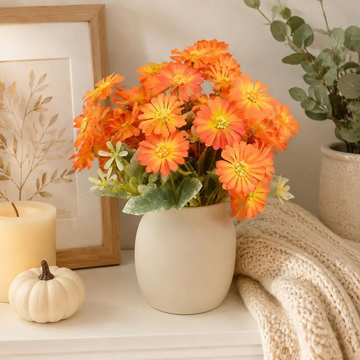 Orange gerbera daisy artificial flowers bouquet in a white vase on a side table with soft natural lighting and home decor