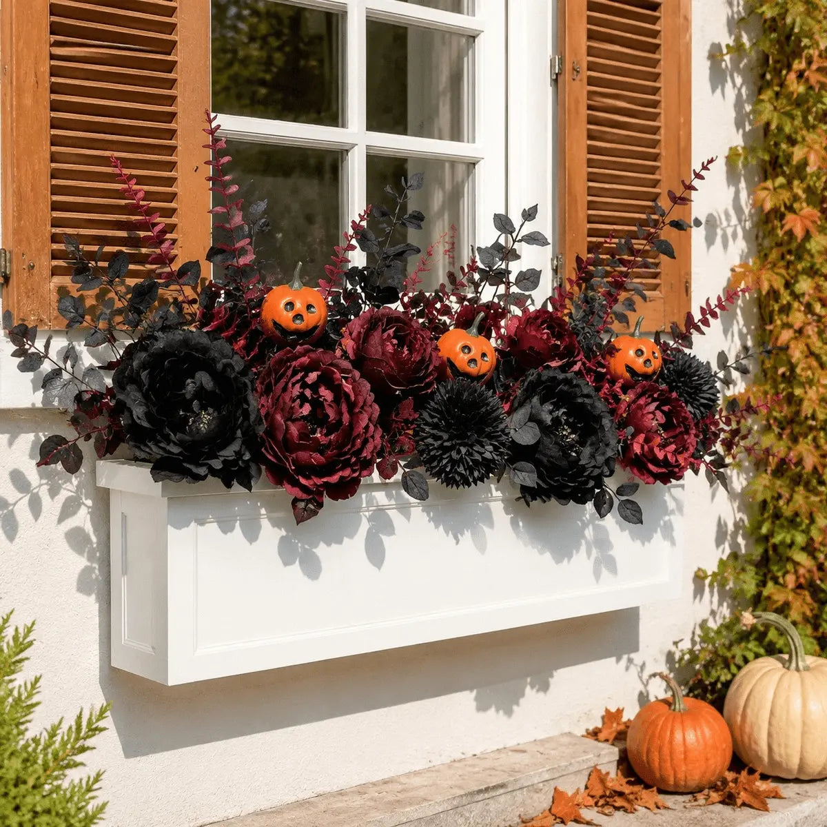 Dark burgundy and black artificial flowers with pumpkin picks arranged in outdoor window box