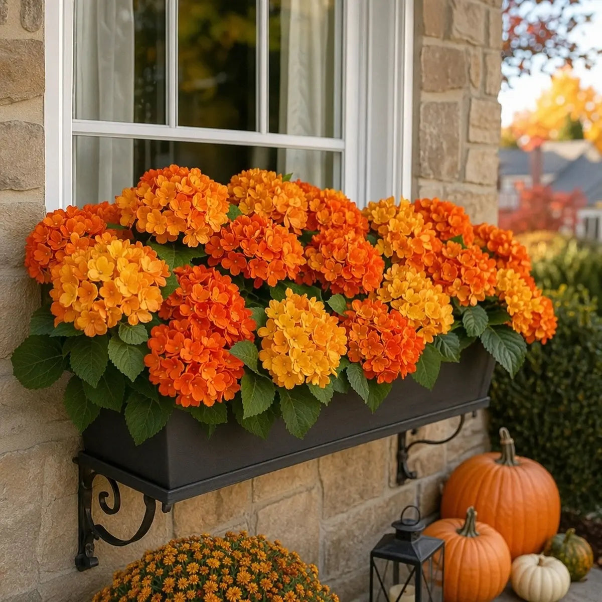 Artificial orange hydrangea stems displayed in a window box planter on a brick wall with pumpkins and fall foliage