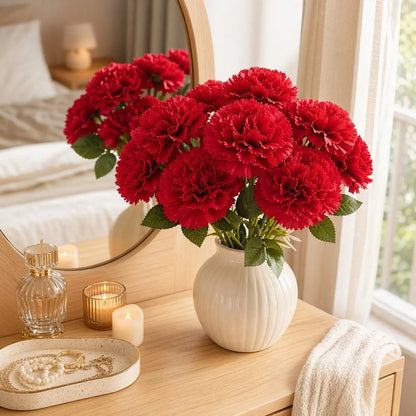 Red artificial carnation flowers in round white ribbed vase on bedroom vanity with candles and jewelry tray, romantic home décor