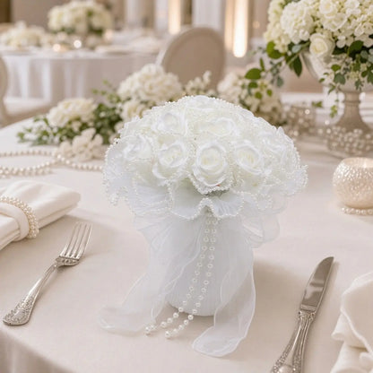 Artificial white rose pearl bead bouquet with organza ribbon placed as centerpiece on white wedding reception dinner table with silverware and candles
