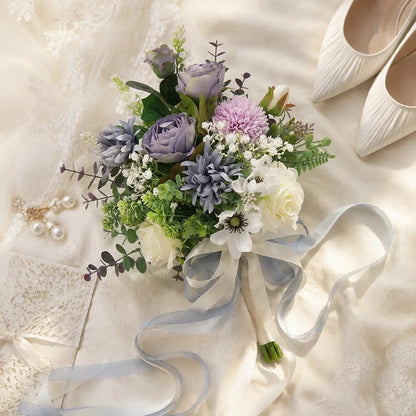 Artificial dusty purple rose white anemone bridal bouquet with satin ribbon flat lay on wedding dress with pearl earrings and heels – IPOPU
