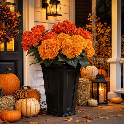 Artificial orange hydrangea stems in a dark vase styled on a porch with lanterns and pumpkins for fall decor
