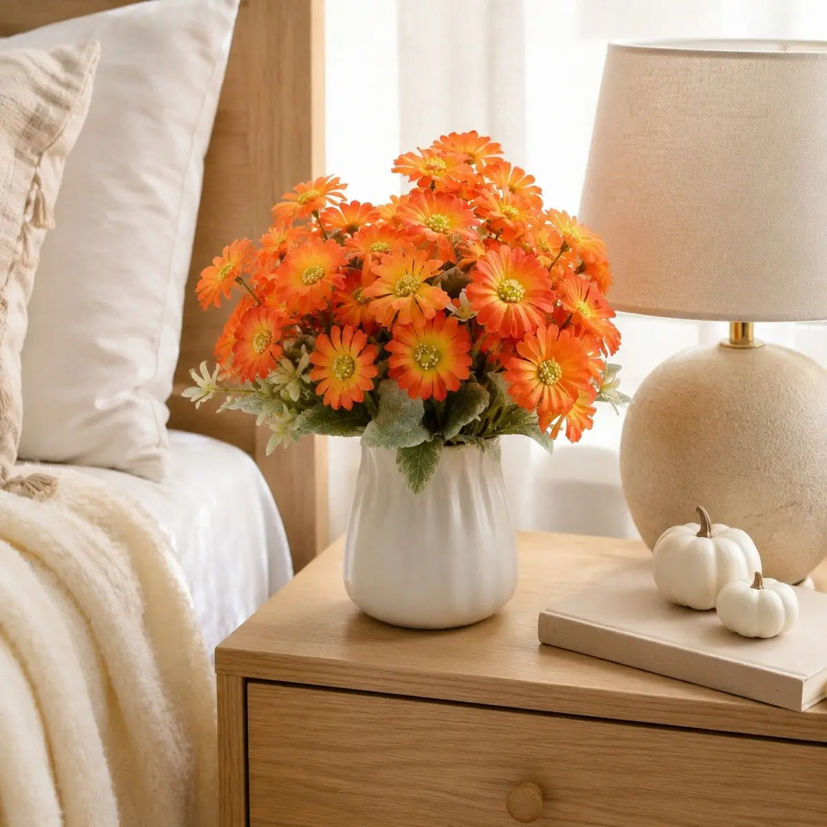 Orange gerbera daisy artificial flowers in a white vase styled on a bedside table in a bright neutral bedroom