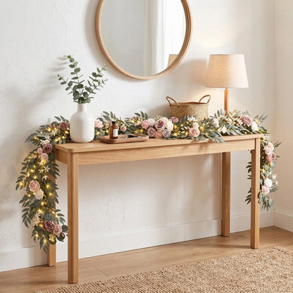 Artificial mauve dusty pink ivory rose eucalyptus garland with warm LED lights draped over natural wood console table in bright home entryway – IPOPU