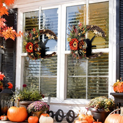 Pair of Halloween crescent moon cat wreaths with sunflowers and fall florals, displayed symmetrically on two outdoor windows with pumpkins and autumn mums below
