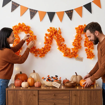Couple arranging orange artificial bougainvillea garland on wall with fairy lights for Halloween party decor, pumpkins and candy on sideboard
