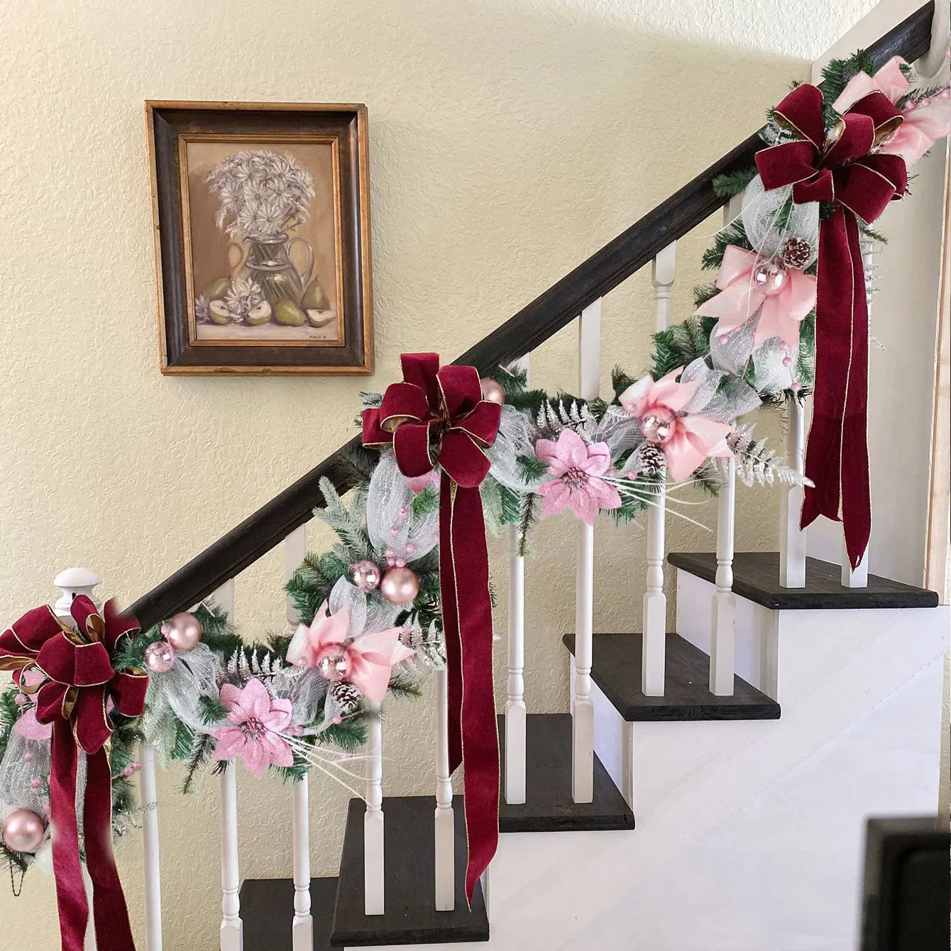 Christmas cane garland with pink poinsettia, mesh ribbon and rose gold ball ornaments, wound along a dark wood staircase railing with burgundy velvet bows, in a warm holiday home interior
