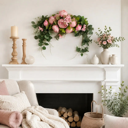 Artificial pink peony eucalyptus arch swag displayed on white fireplace mantel with wood candlestick holders and cream vases in cozy living room