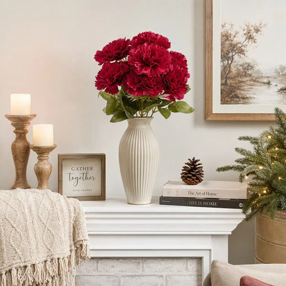 Faux red carnation artificial flowers in white vase on farmhouse mantel shelf with candles and pinecone, cozy home décor