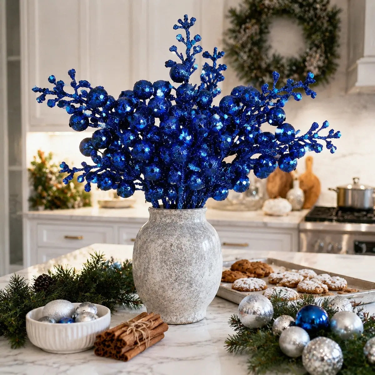 20 pack glitter blue artificial berry stems arranged as a vase filler in a white speckled ceramic vase on a marble kitchen island, surrounded by pine branches, cinnamon sticks, silver and blue ball ornaments and Christmas cookies for a festive winter holiday display
