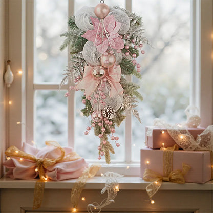 27.6 inch pink Christmas teardrop swag with glitter poinsettia, mesh bow, rose gold ball ornaments and pine cone, hung in a window with fairy lights and pink gift boxes
