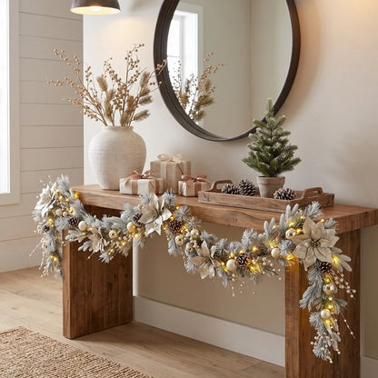 5.9FT frosted Christmas garland with champagne poinsettia, gold ball ornaments and pearl berries with warm fairy lights, draped along a rustic wood console table styled with wrapped gifts, mini Christmas tree and white ceramic vase in a modern farmhouse entryway
