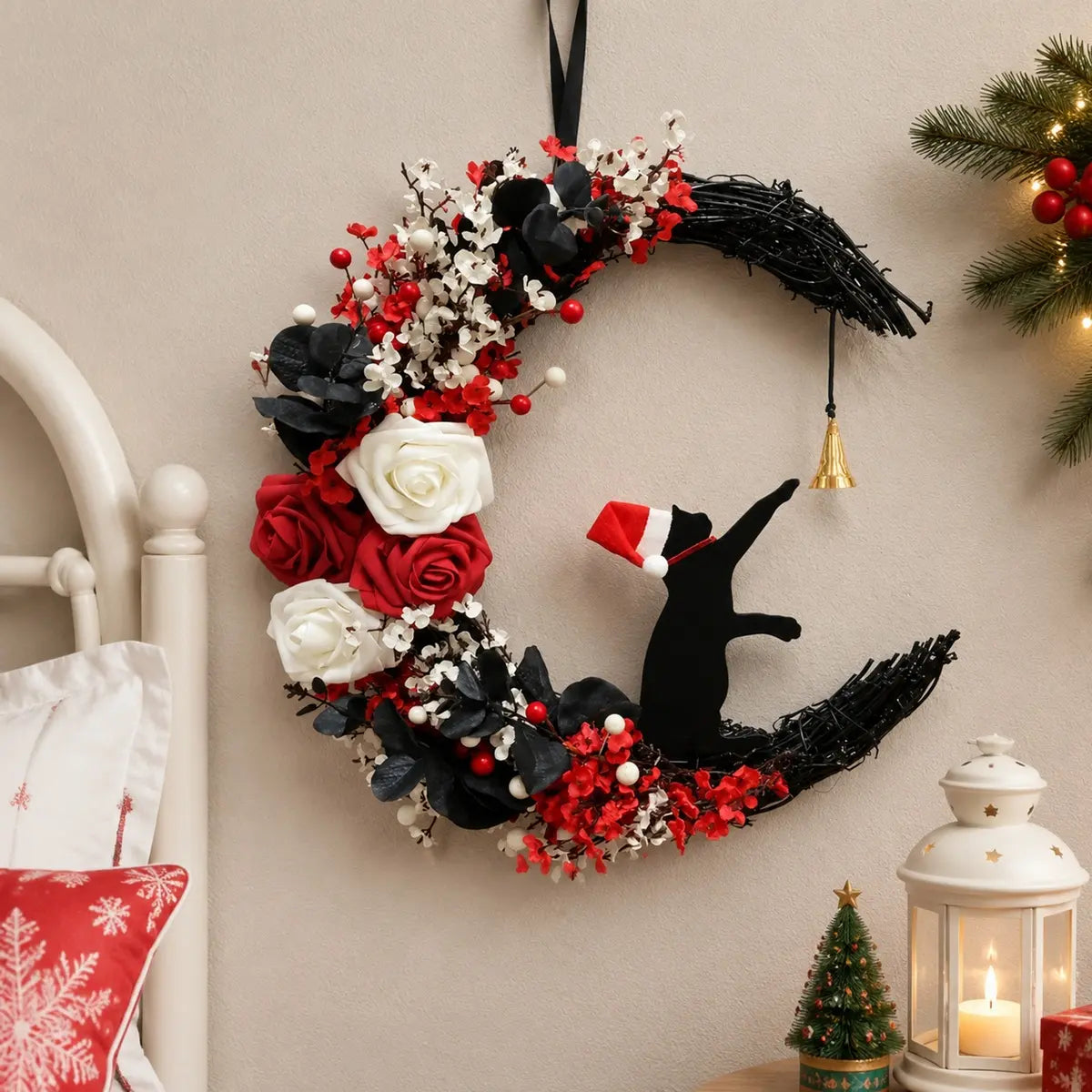 Christmas black cat moon wreath with white and red roses, red berries, white blossoms and gold jingle bell, hung on bedroom wall beside white bed headboard with Christmas lantern and mini tree