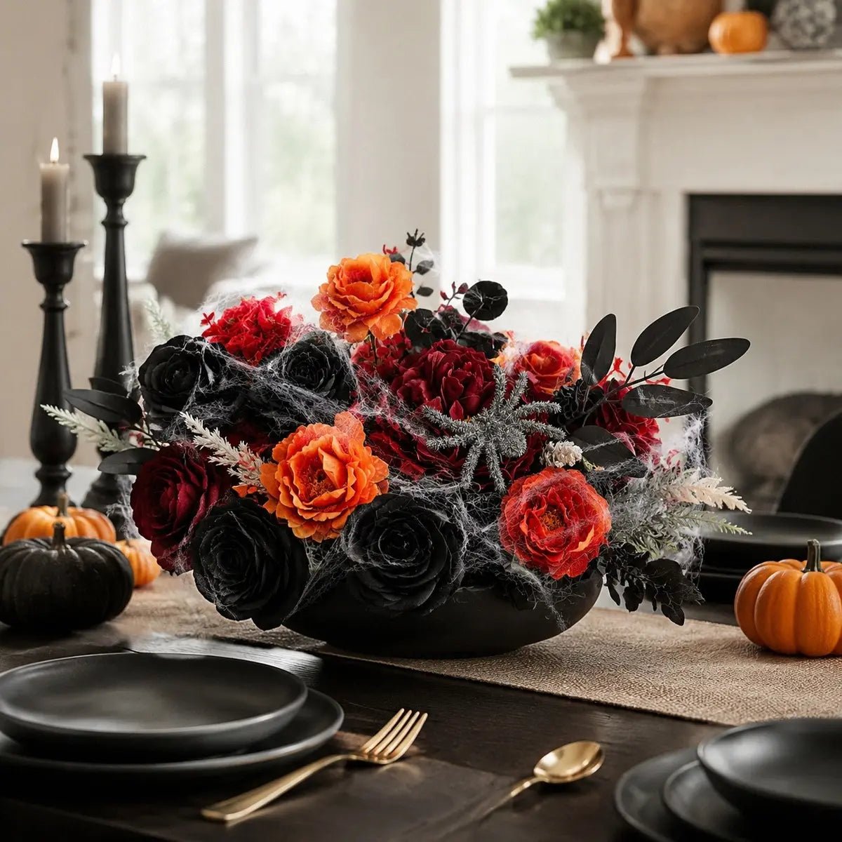 Orange black red artificial peonies and roses combo arranged in a low black bowl as a Halloween dining table centerpiece with black plates, gold cutlery, black candlesticks, and mini pumpkins