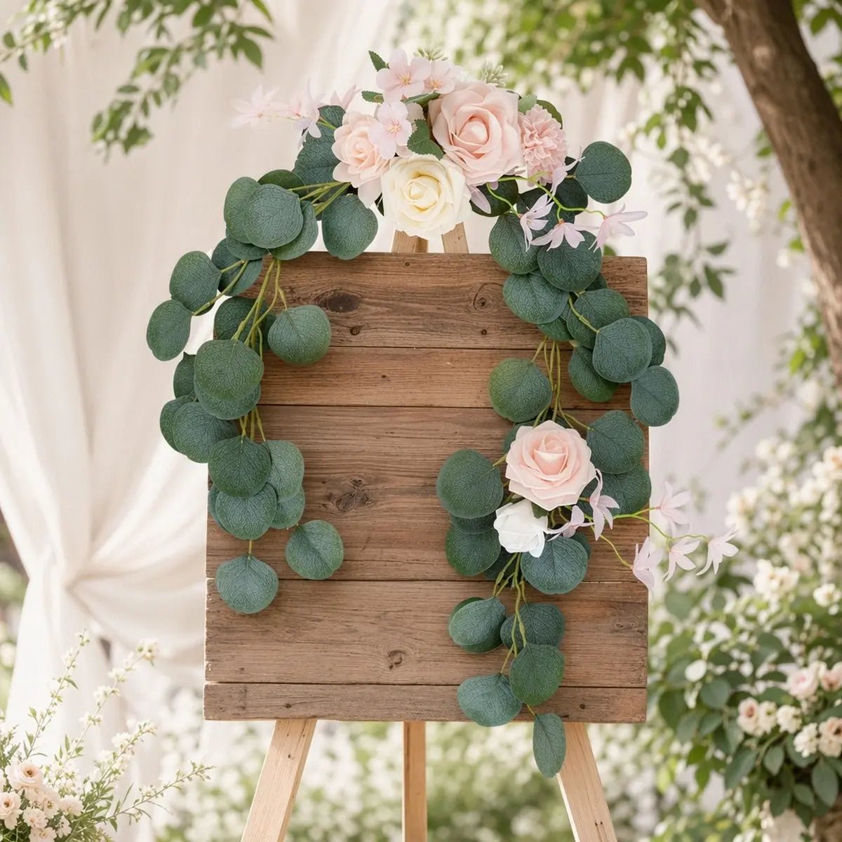 Blush pink rose silver dollar eucalyptus chair swag set of 2 styled diagonally on rustic wood easel welcome sign at outdoor garden wedding with white drape backdrop – IPOPU