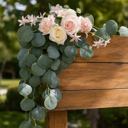 Blush pink and cream rose silver dollar eucalyptus chair swag draped over rustic wood square arch beam in outdoor garden wedding ceremony close-up view – IPOPU