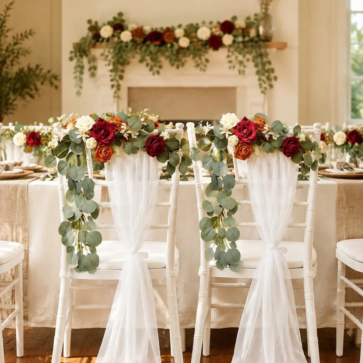 Artificial burgundy orange ivory rose eucalyptus garland on white Chiavari chairs at indoor wedding reception – IPOPU
