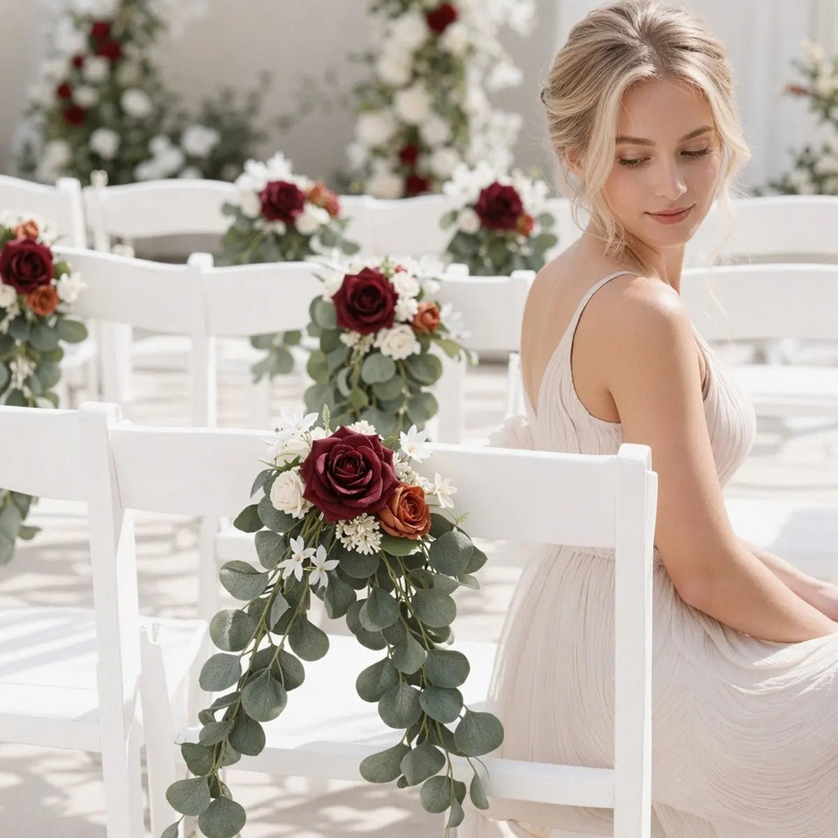 Burgundy terracotta rose silver dollar eucalyptus chair swag hanging on white folding aisle chair back with bride in soft focus at indoor wedding ceremony – IPOPU