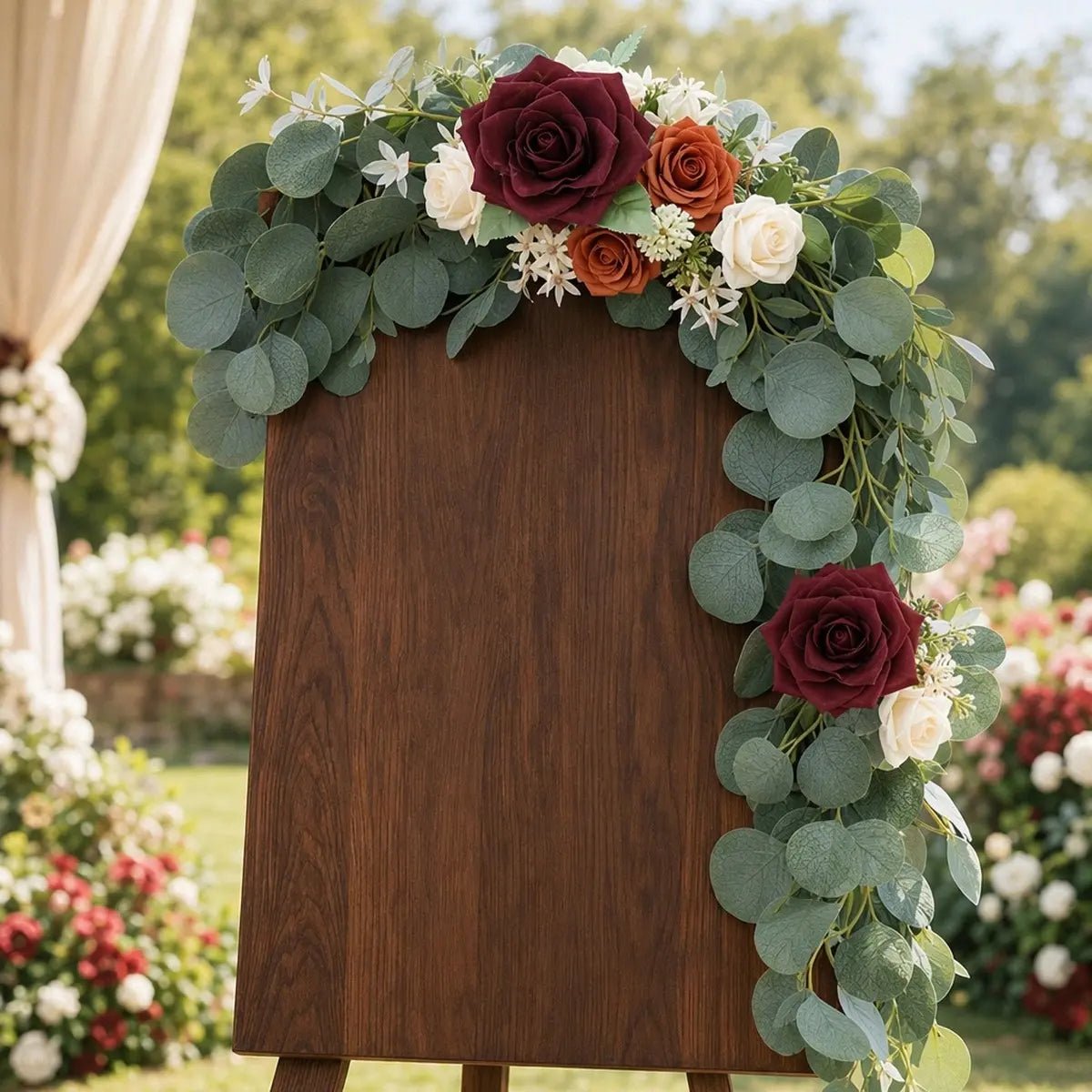 Burgundy terracotta rose silver dollar eucalyptus swag set of 2 draped over top and right side of dark wood easel welcome sign in outdoor rose garden wedding – IPOPU