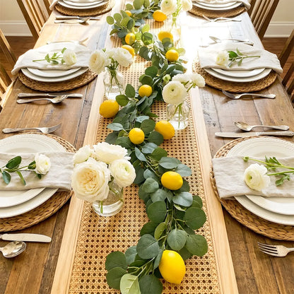 Artificial lemon greenery garland laid along formal dining table centerpiece with white ranunculus flowers and cane table runner, wedding table décor
