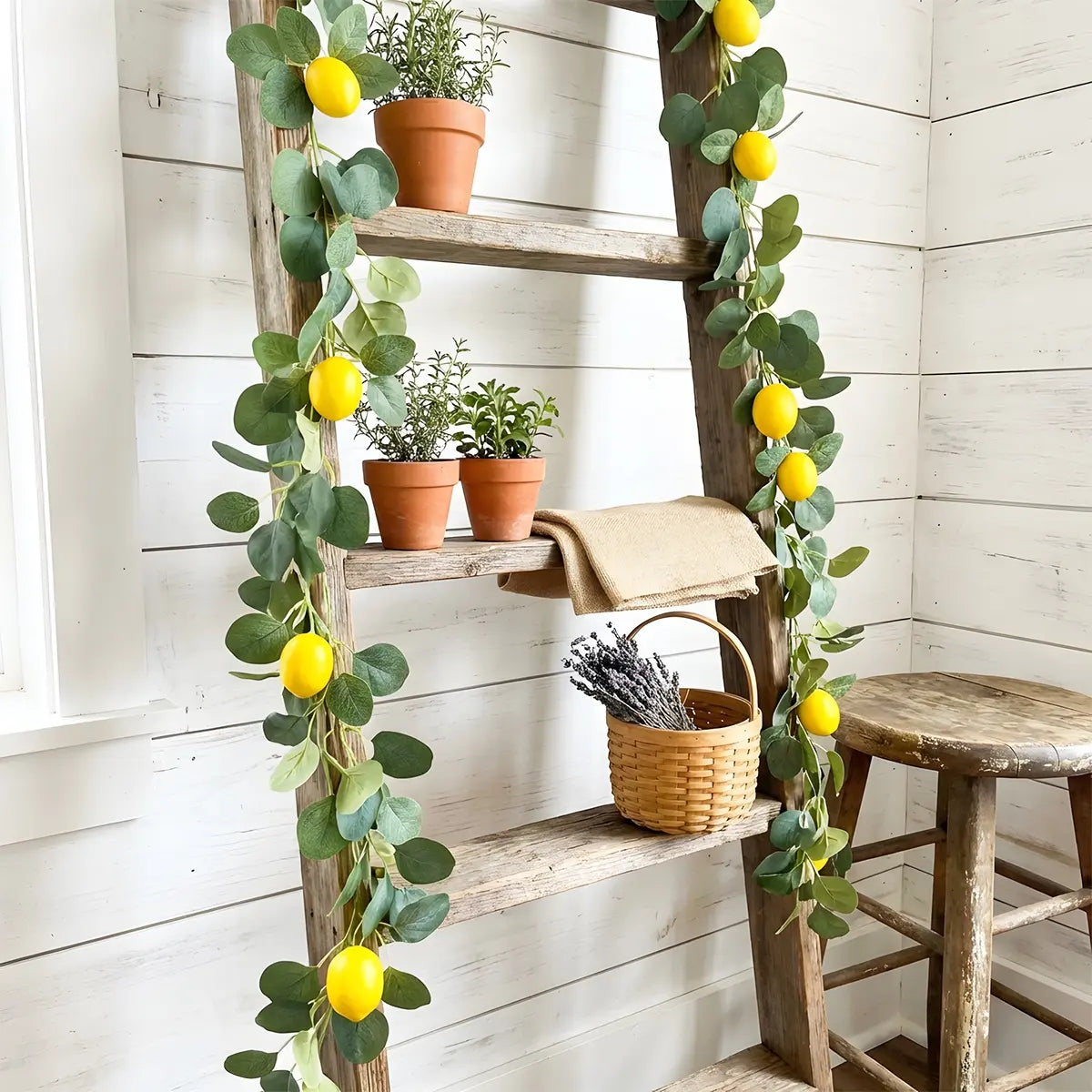 Artificial lemon eucalyptus garland wrapped around rustic wooden ladder shelf with terracotta herb pots and wicker basket, farmhouse home décor