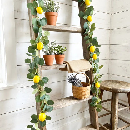 Artificial lemon eucalyptus garland wrapped around rustic wooden ladder shelf with terracotta herb pots and wicker basket, farmhouse home décor