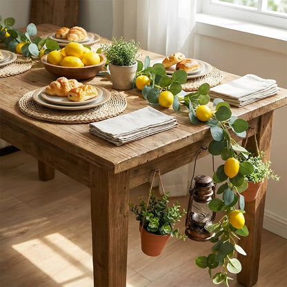 Artificial lemon greenery garland laid along formal dining table centerpiece with white ranunculus flowers and cane table runner, wedding table décor