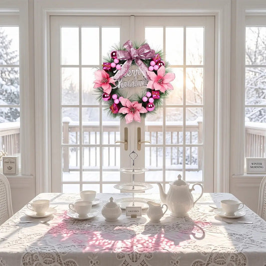 Pink Christmas pine wreath with pink poinsettia blooms, hot pink ball ornaments, pink berry clusters, mini gift boxes and glitter pink bow knot with Merry Christmas sign, hung on a white French door overlooking a snowy winter garden, above a white lace tablecloth tea table set with white porcelain teapot and cups