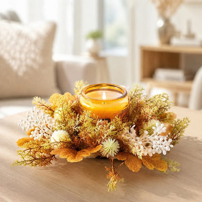 Neutral fall candle ring wreath with cream berries, thistle and golden maple leaves arranged around an amber glass candle on a white marble surface