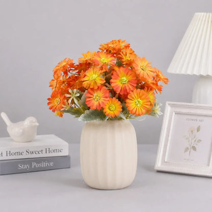 Orange gerbera daisy artificial flowers bouquet arranged in a white ceramic vase on a desk with books and home decor
