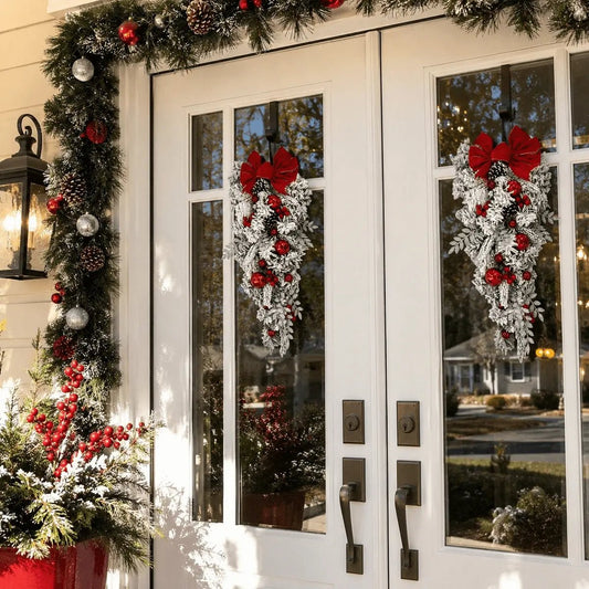 Flocked Christmas teardrop swag with red bow, ornaments and pinecones hung on a white front door for holiday entryway decor