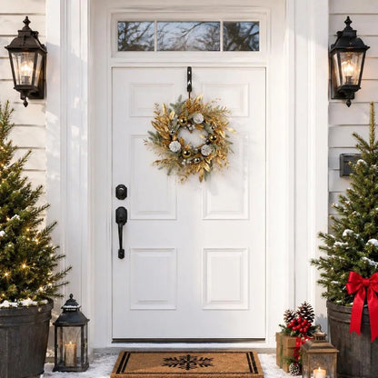 19.7 inch gold Christmas wreath with gilded golden leaves, gold and silver ball ornaments and white frosted pinecones, hung on a white six-panel front door with a black iron hook, flanked by two lit potted Christmas trees in dark metal planters with a black lantern and pine cone arrangement, on a white farmhouse porch with a snowflake doormat in winter