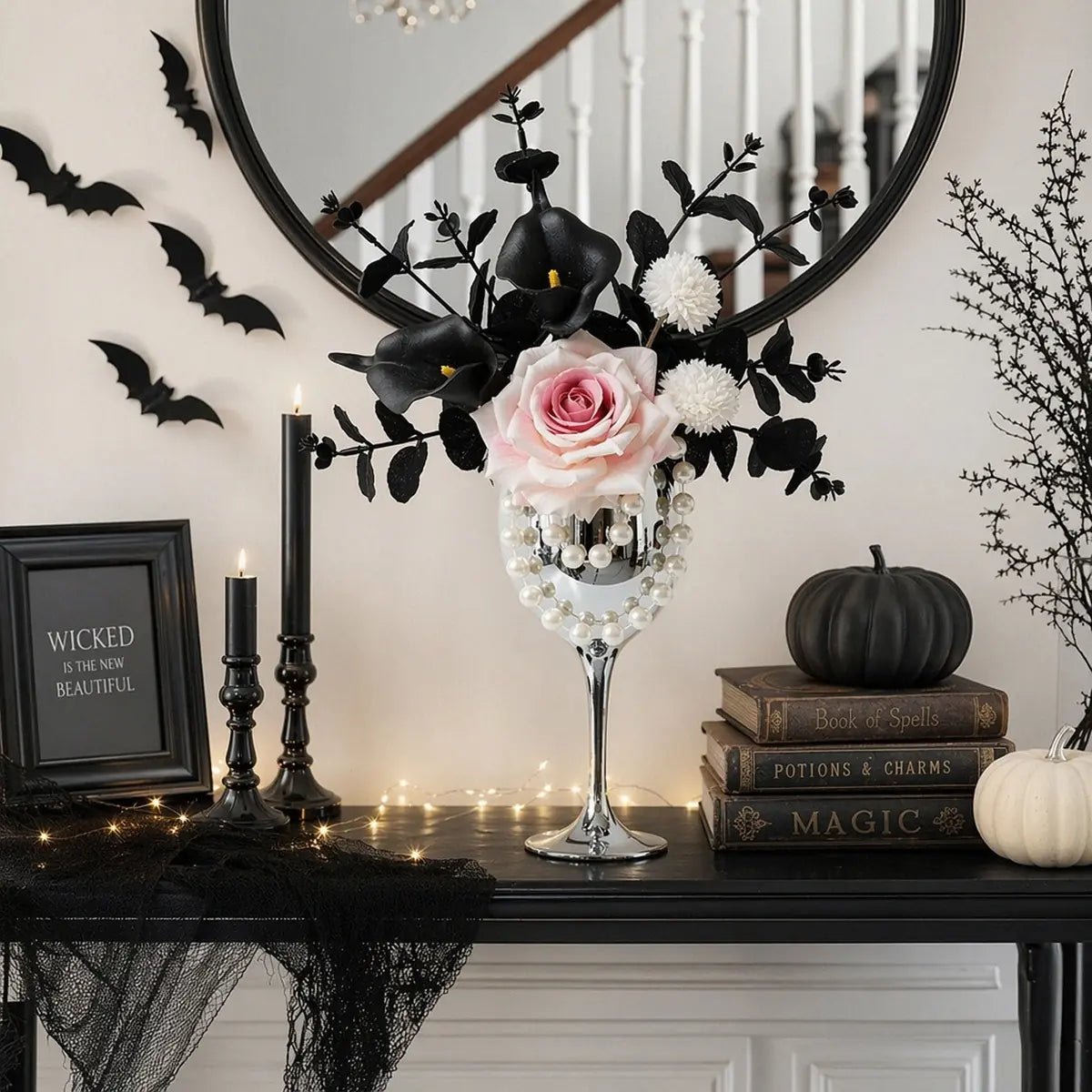 White and black gothic artificial flower arrangement with black calla lilies in silver goblet vase on a dark shelf with bat wall decorations