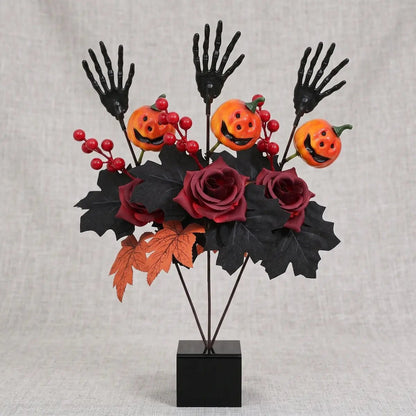 Halloween skeleton hand artificial flower arrangement with black roses, pumpkin faces and maple leaves in a black vase
